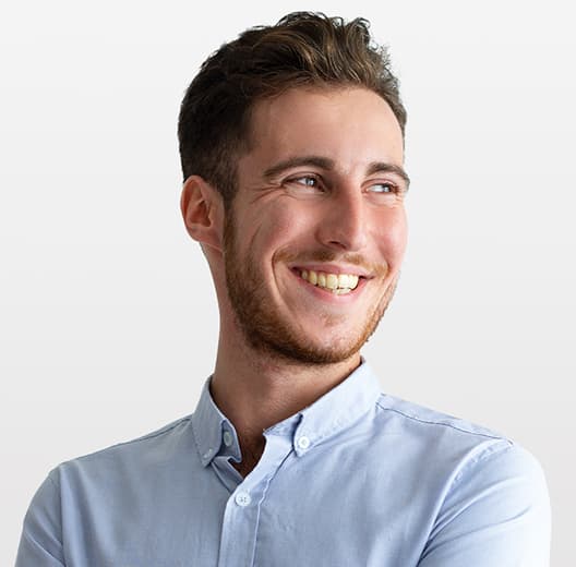 a grinning man with moustache, small beard, brown hair, brown eyes in blue shirt