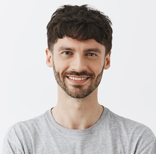 a grinning man with stubble, brown hair, brown eyes in a gray t-shirt